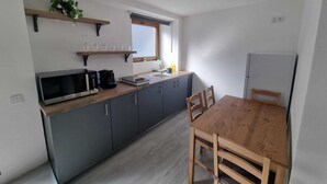 Et lille køkken med mikrobølgeovn, kaffemaskine og et træspisebord med stole.