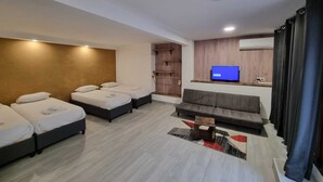Et moderne hotelværelse med sofa, to enkelt senge, et fjernsyn og et lille bord.