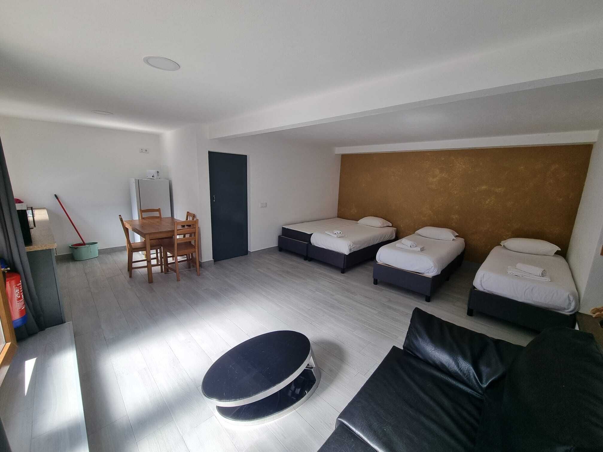 Ett modernt hotellrum med två separata sängar, en soffa, ett matbord med stolar och ett litet pentry.
