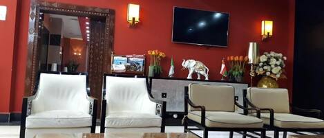 A lobby with a red wall, a large mirror, a flat-screen TV, and seating arrangements including white and beige chairs.