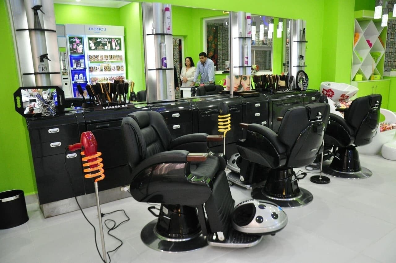 A salon with multiple black salon chairs, a counter with various hair products, and a green wall.