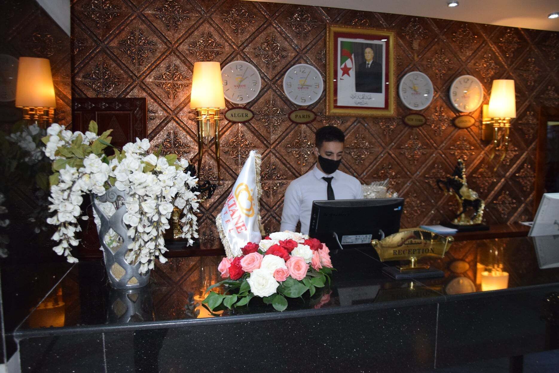 A reception desk with a clock, a framed portrait, and a bouquet of flowers.