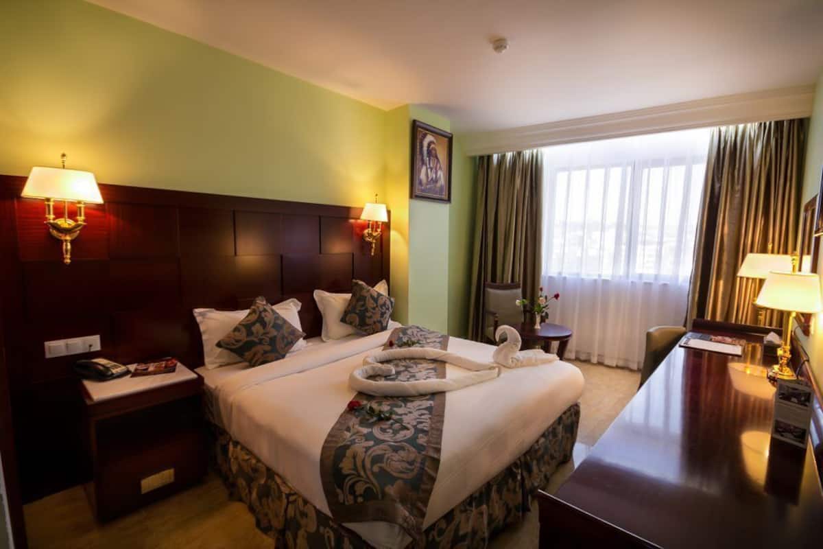 A hotel room with a large bed, two bedside lamps, a desk, and a window with curtains.