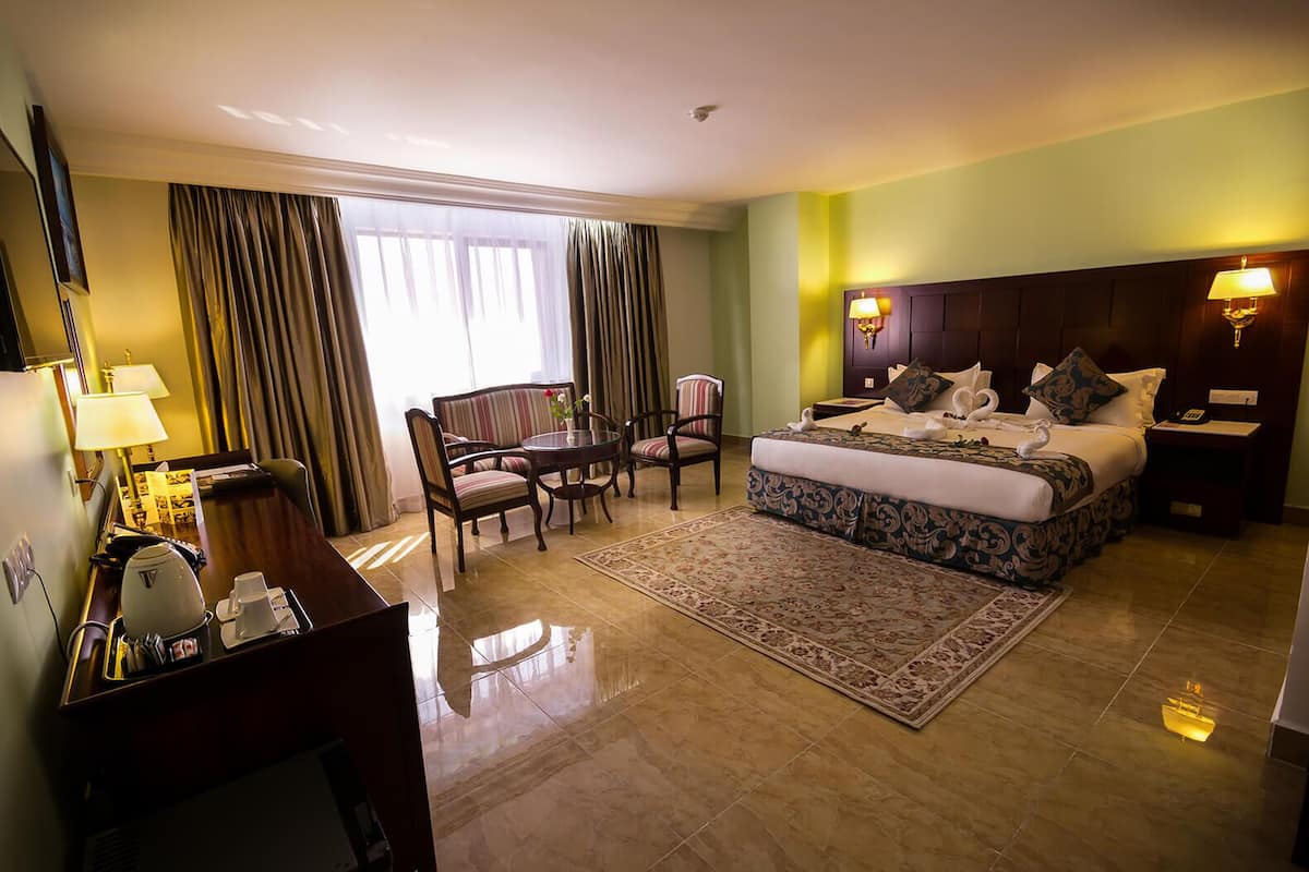 A hotel room with a bed, a desk with a telephone, a chair, a table, and a window with curtains.
