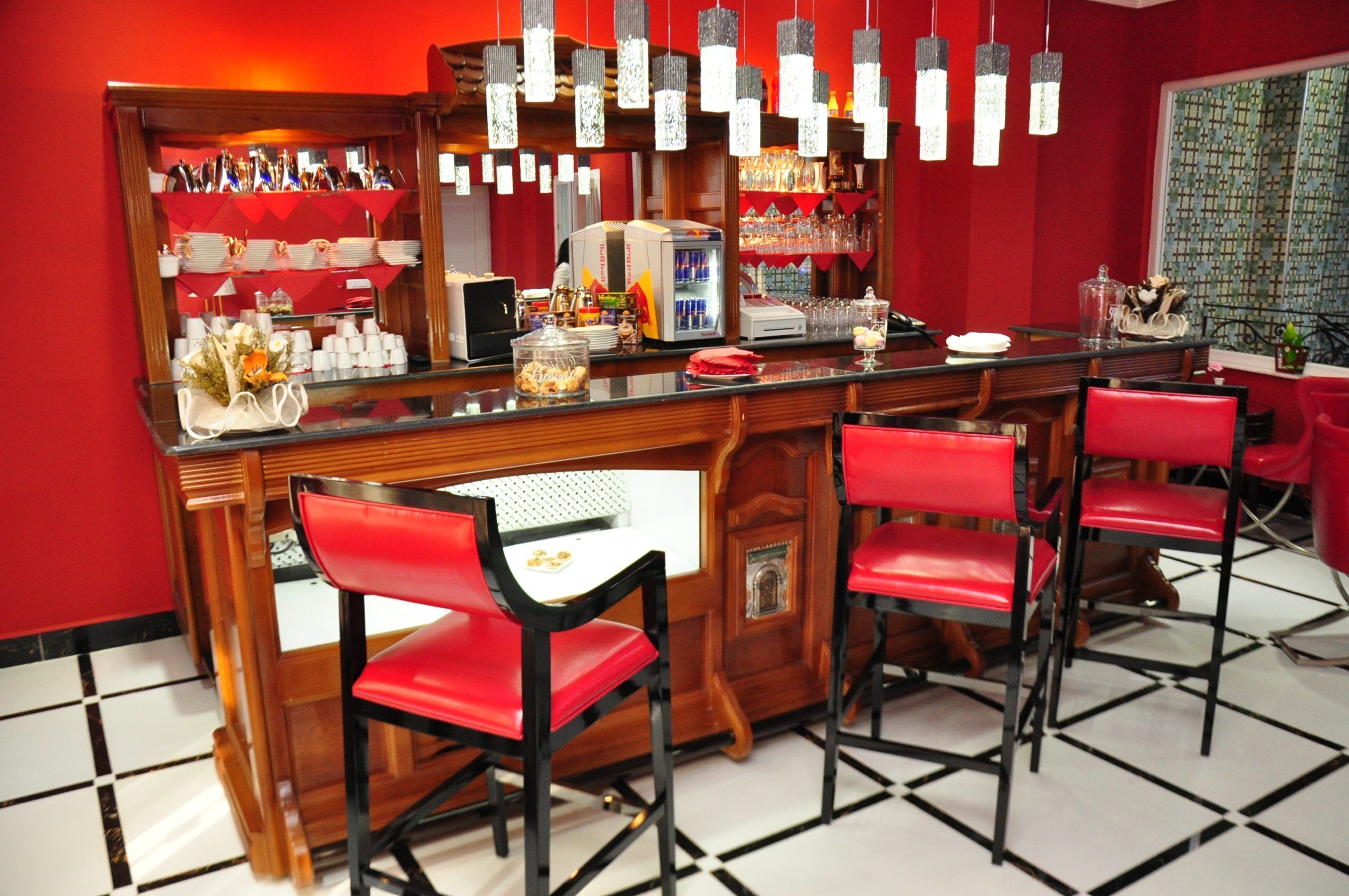 A bar area with red chairs, a counter with various items, and hanging lights.