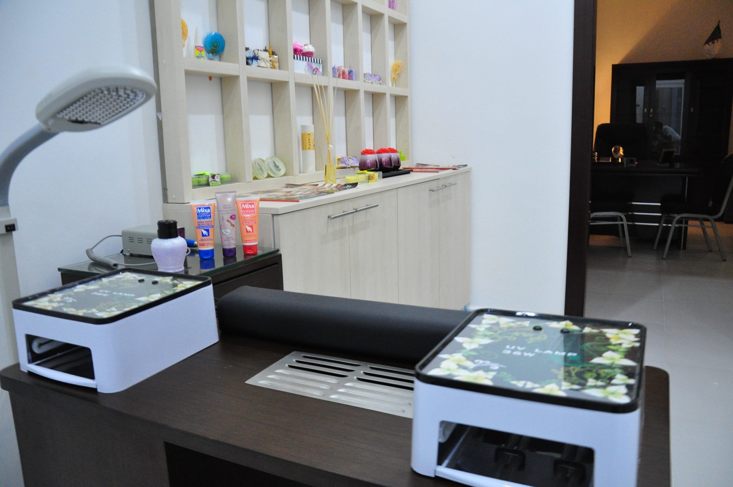 A reception desk with a desk lamp, a computer, and a shelf with various items.