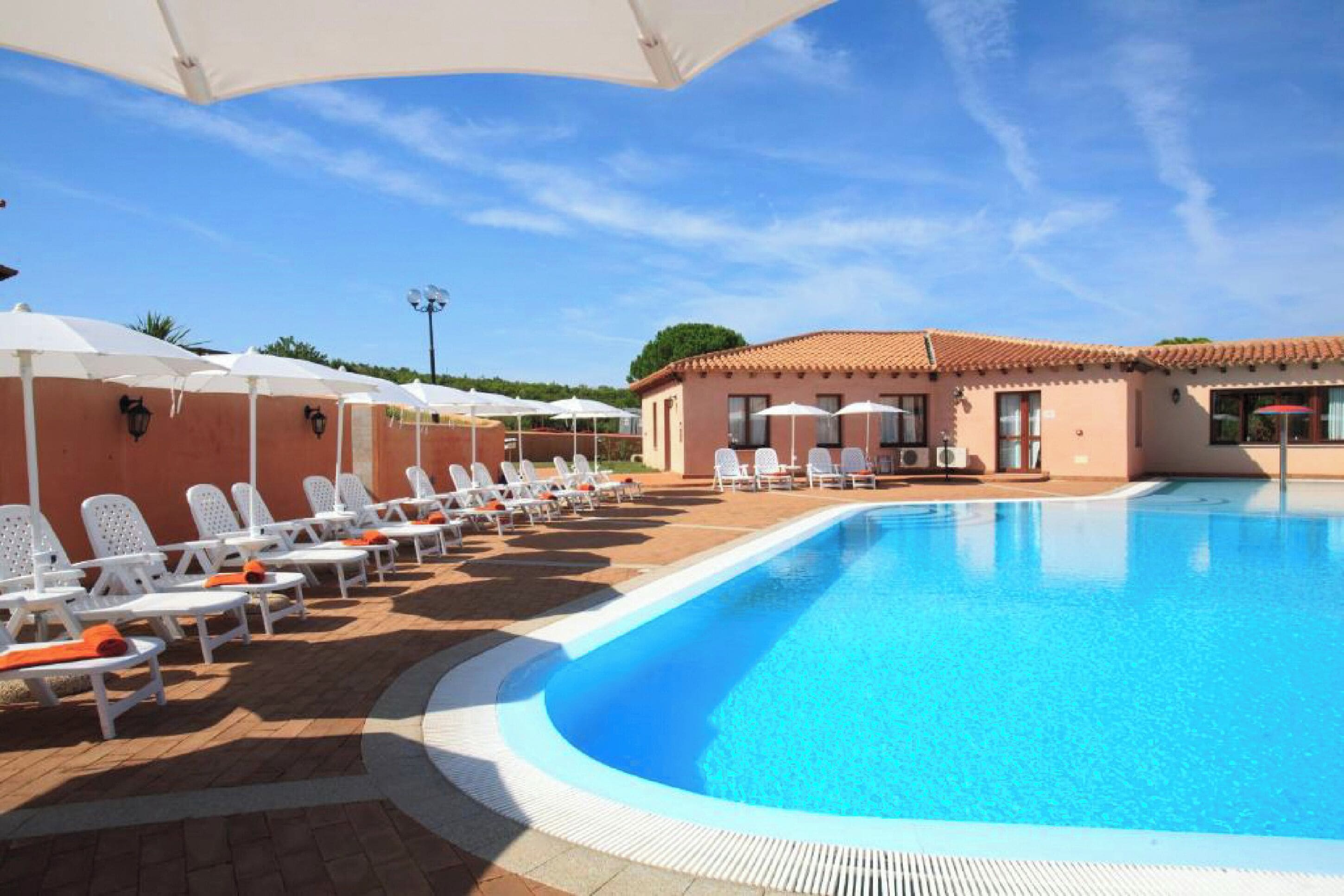 A swimming pool with lounge chairs and umbrellas, surrounded by a building with a tiled roof.