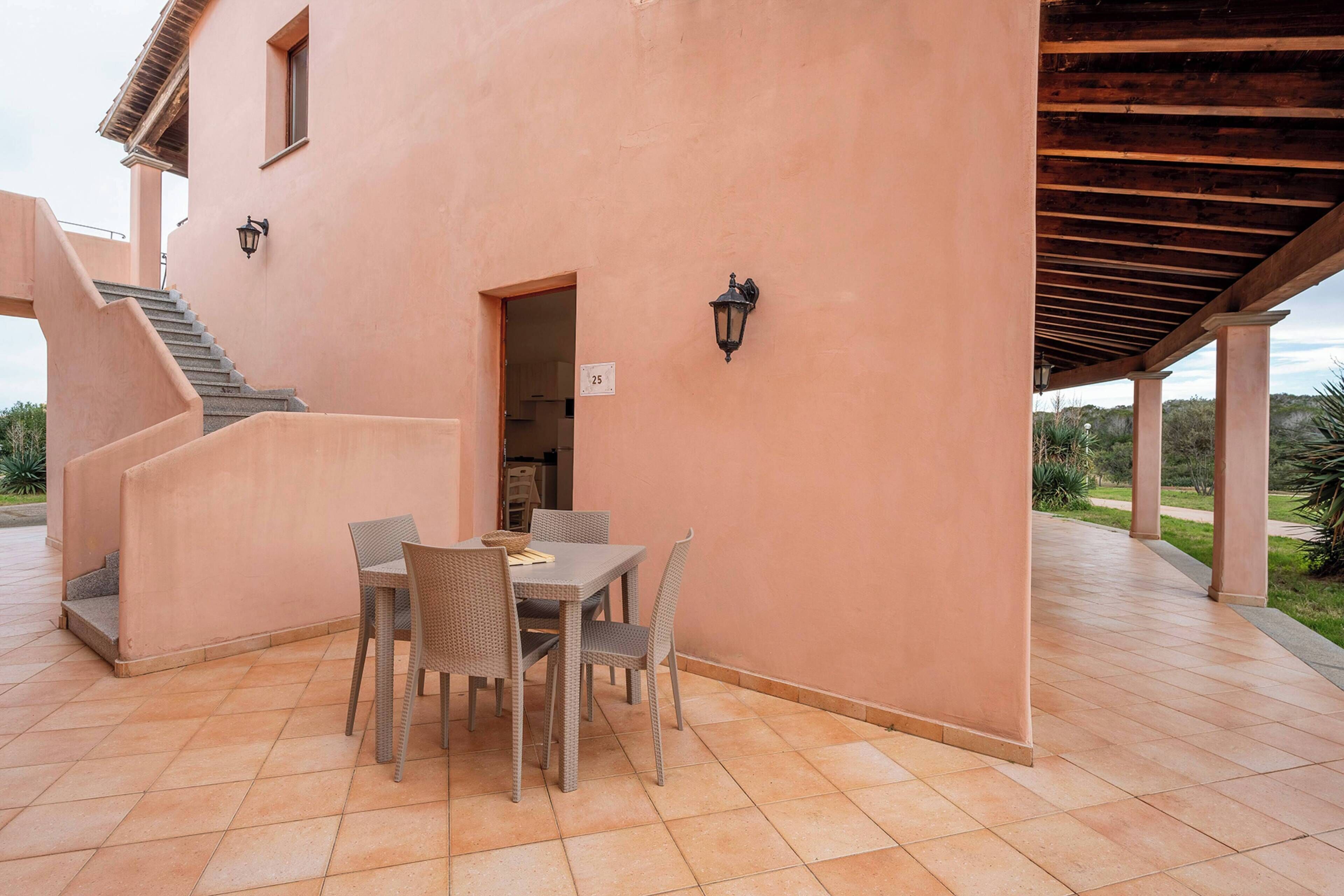 A covered patio with a table and chairs, a staircase, and a building exterior.