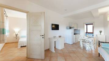 A room with a bed, a desk, a dining table with chairs, a TV, and a kitchenette.