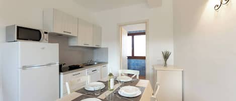 A modern kitchen with white appliances, a dining table set for four, and a view into the living area.