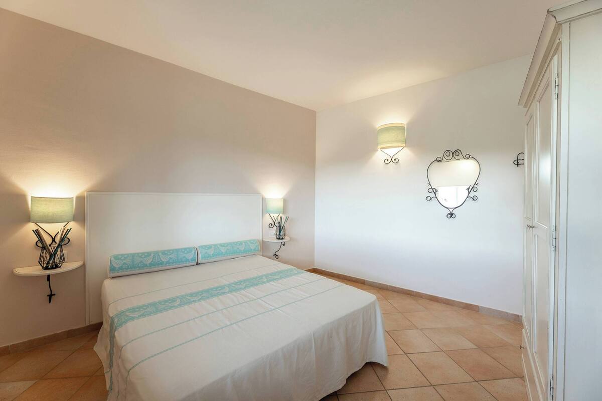Een slaapkamer met een bed, twee wandlampen, een nachtkastje met een lamp en een spiegel aan de muur.