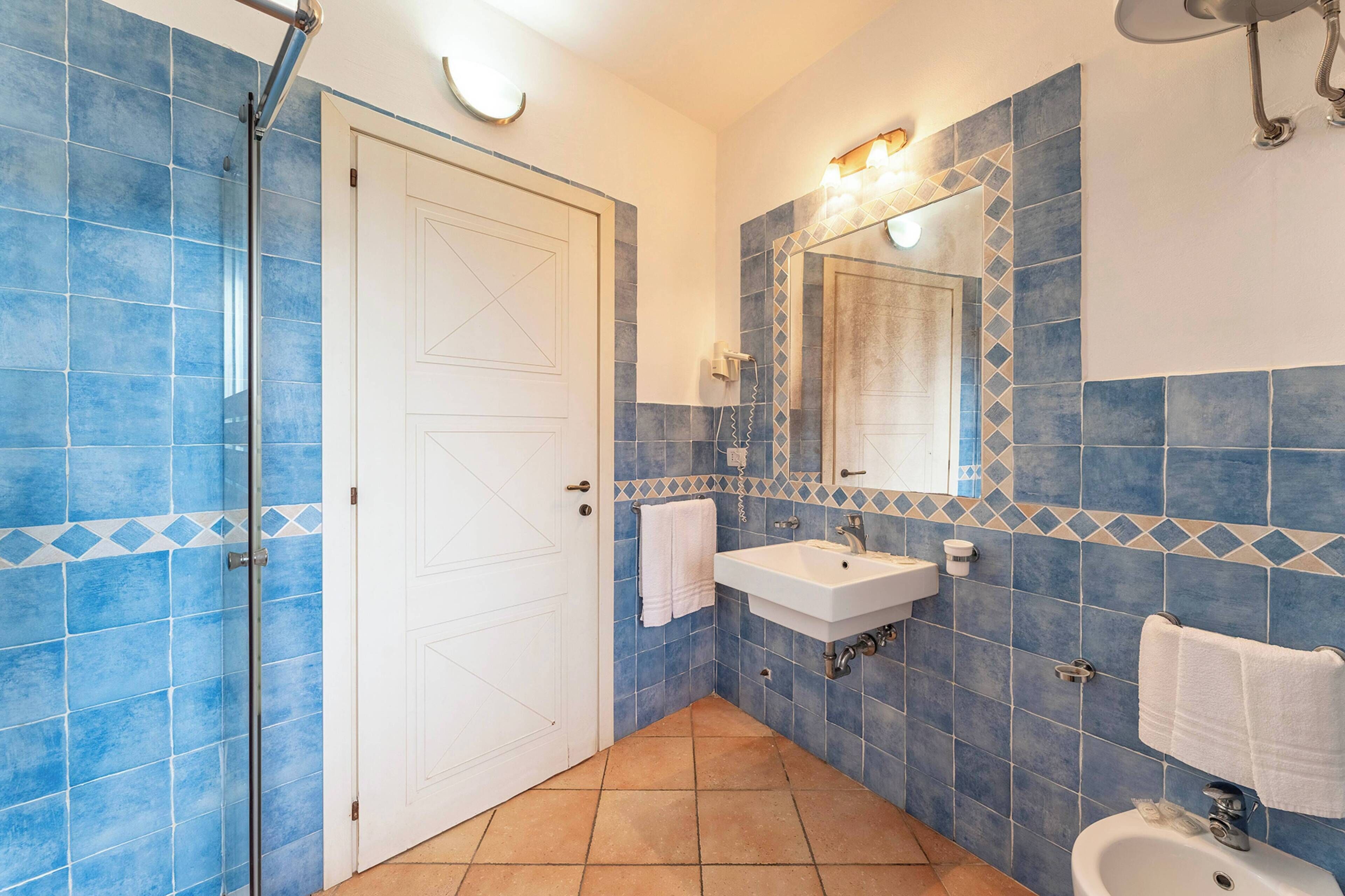 A bathroom with blue tiles, a white sink, a mirror, and a shower.