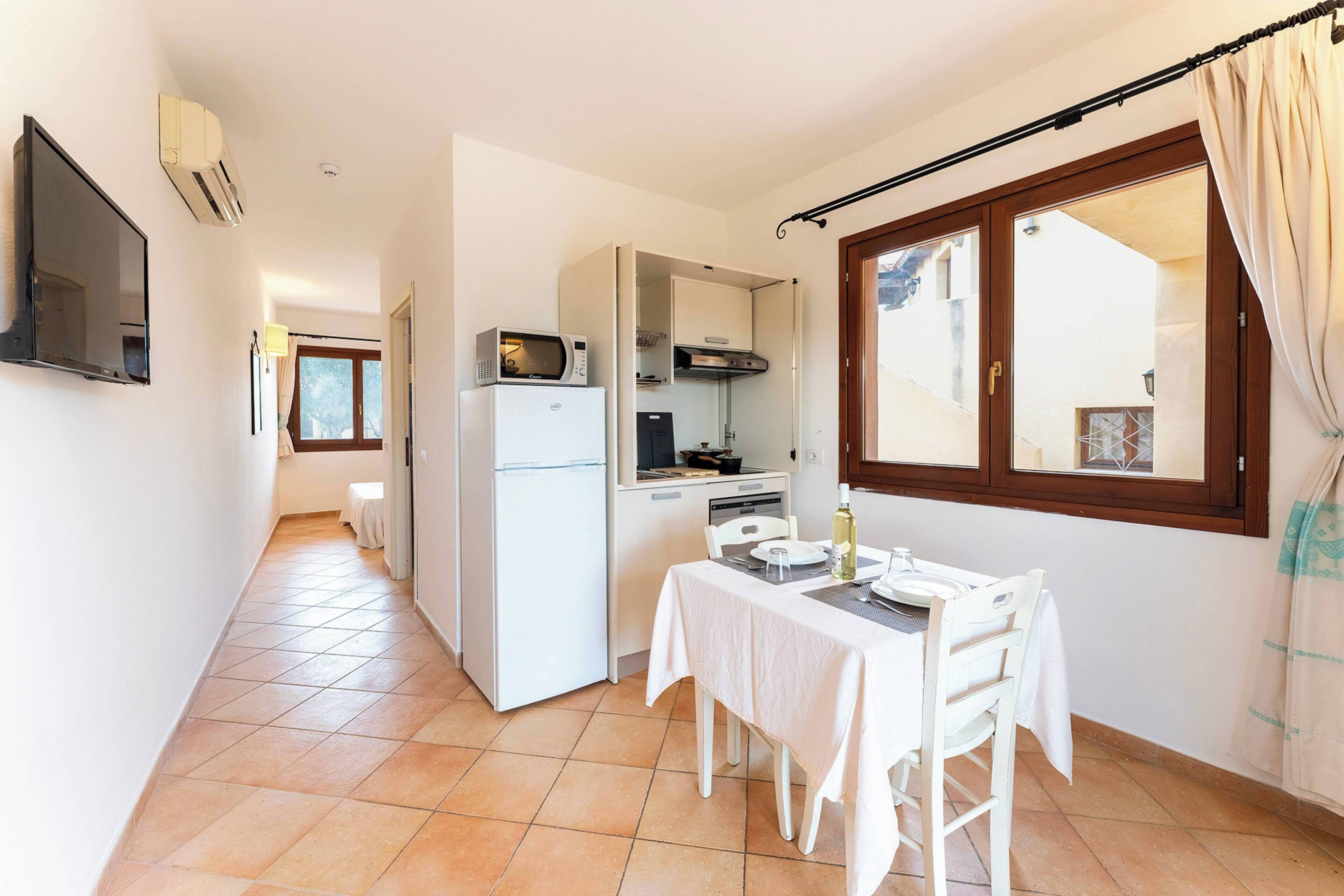 A compact kitchen with a refrigerator, microwave, and stove, a dining table with chairs, and a window with curtains.