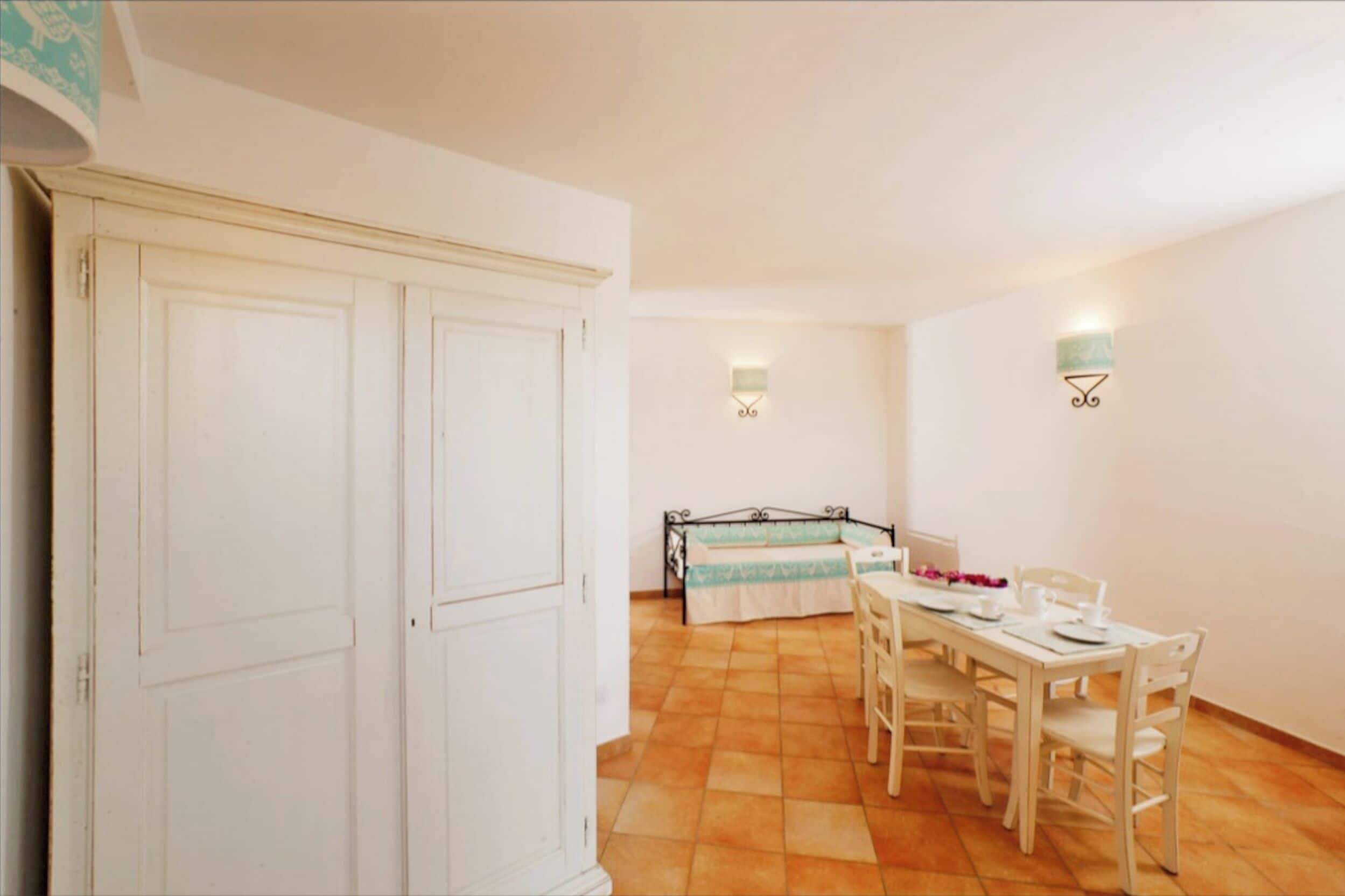 A room with a dining table set for four, a bed with a blue and white bedspread, and a white wardrobe.