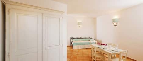 Una habitación con una mesa de comedor preparada para cuatro personas, una cama con colcha azul y blanca, y un armario blanco.