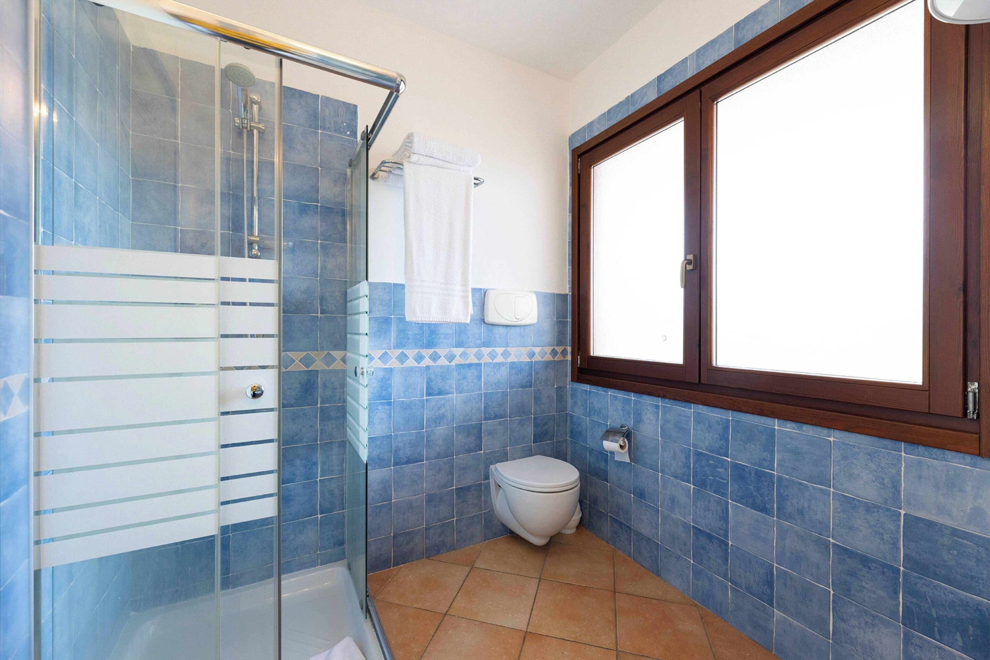 A bathroom with a glass shower enclosure, a toilet, and a window.