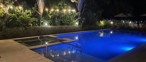A nighttime swimming pool area with a clear pool, steps leading into the water, and surrounding greenery.