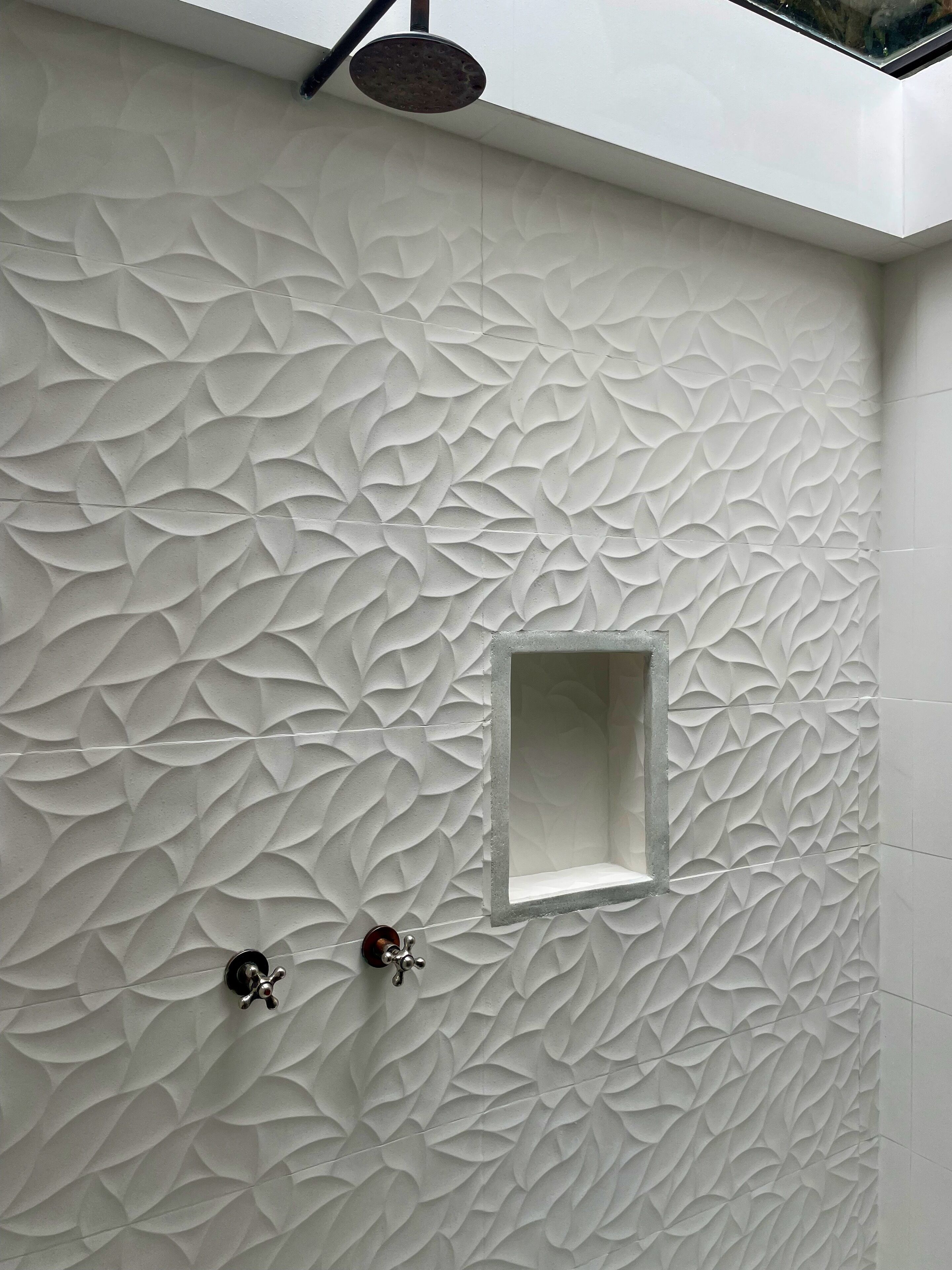 A bathroom with a textured wall, a small window, and a showerhead.