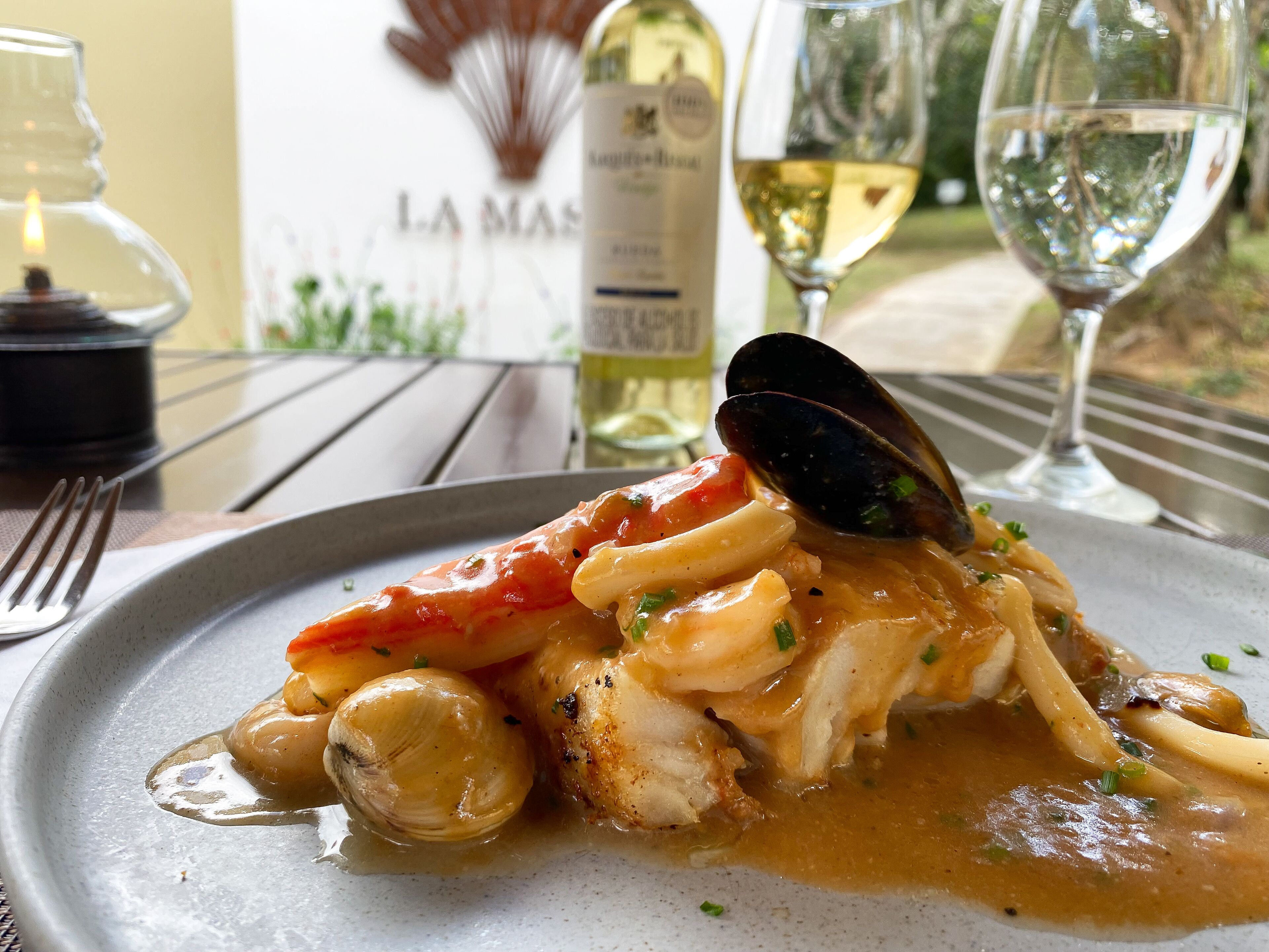 A seafood dish on a plate with a bottle of wine and glasses in the background.