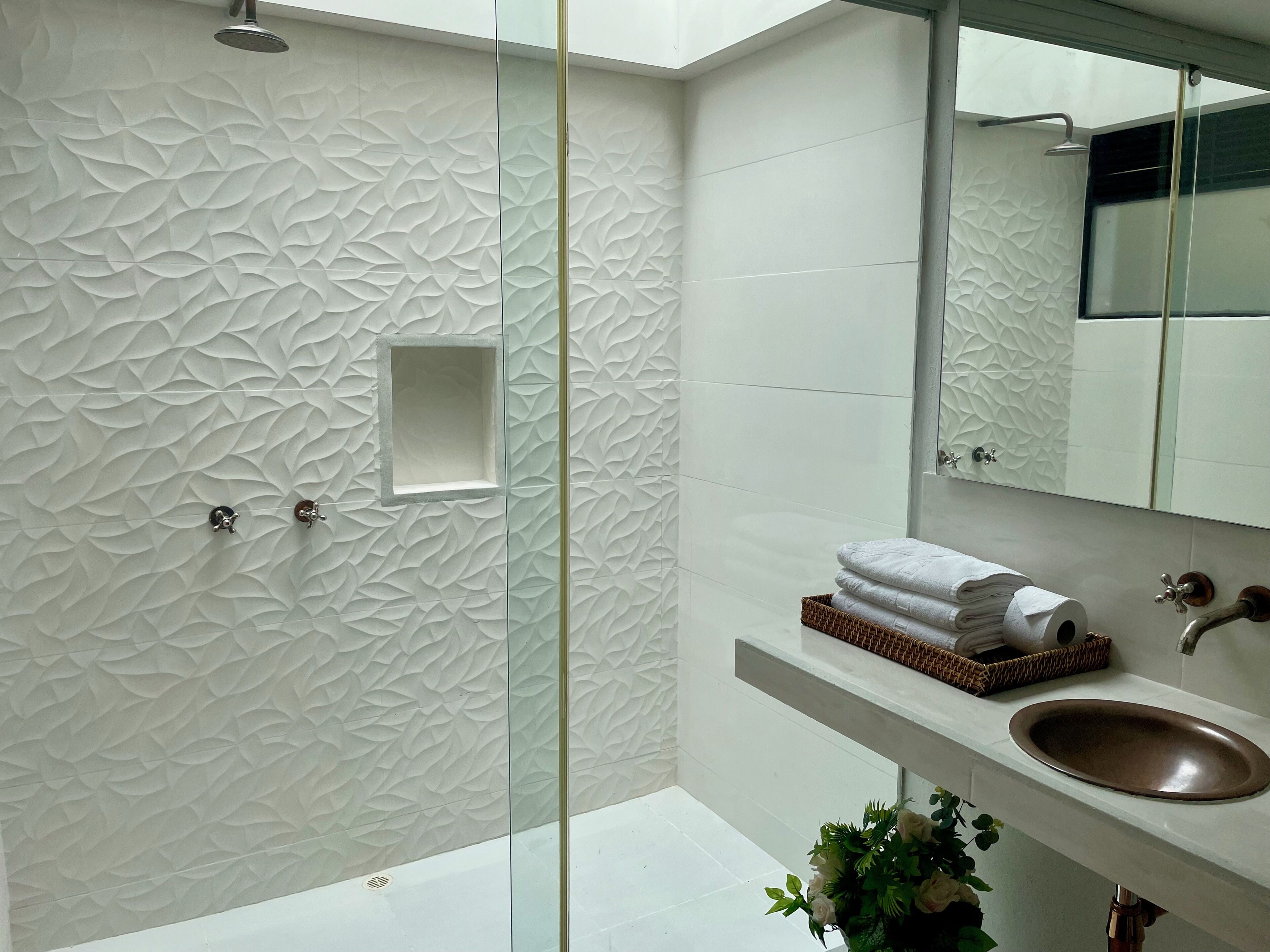 A modern bathroom with a textured wall, a glass shower enclosure, a sink with a brown basin, and a mirror above the sink.