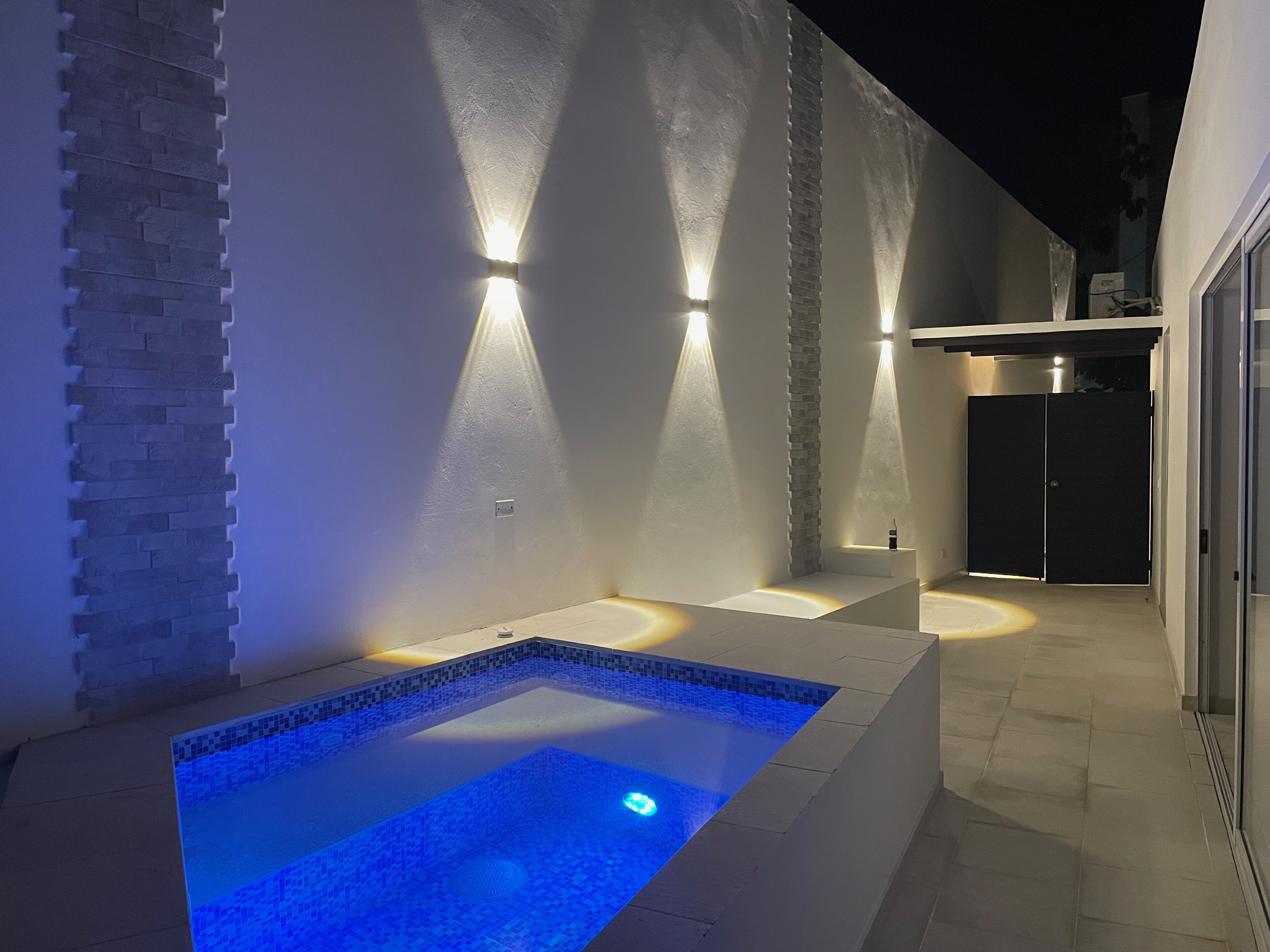 A modern outdoor pool area with a rectangular pool, two sunken seating areas, and a stone accent wall.