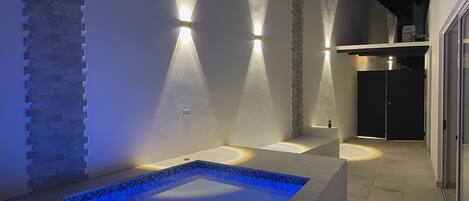 A modern outdoor pool area with a rectangular pool, two sunken seating areas, and a stone accent wall.