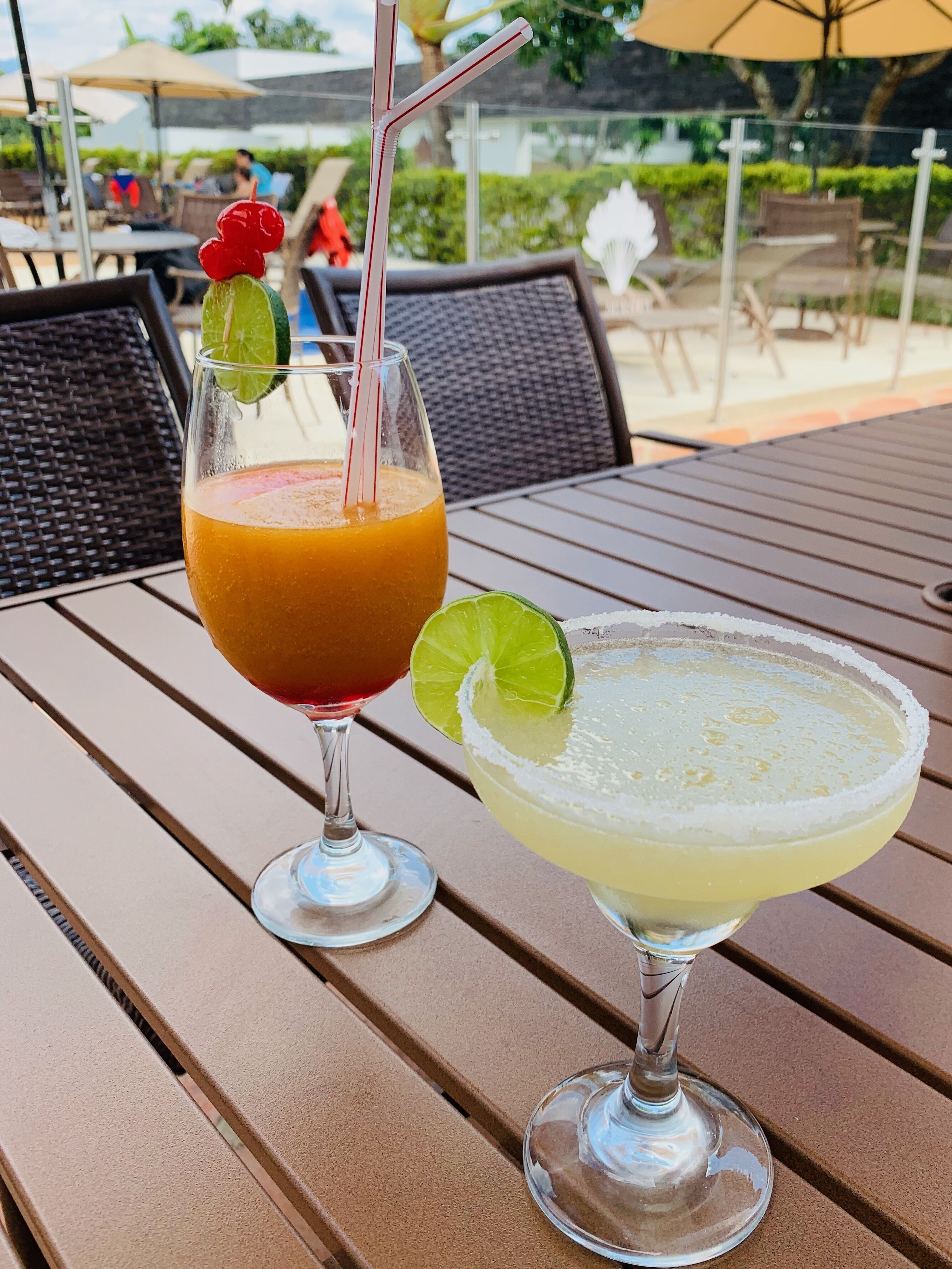 Duas bebidas sobre uma mesa, com vista para área externa e guarda-sóis.