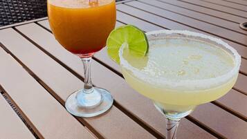 Duas bebidas sobre uma mesa, com vista para área externa e guarda-sóis.