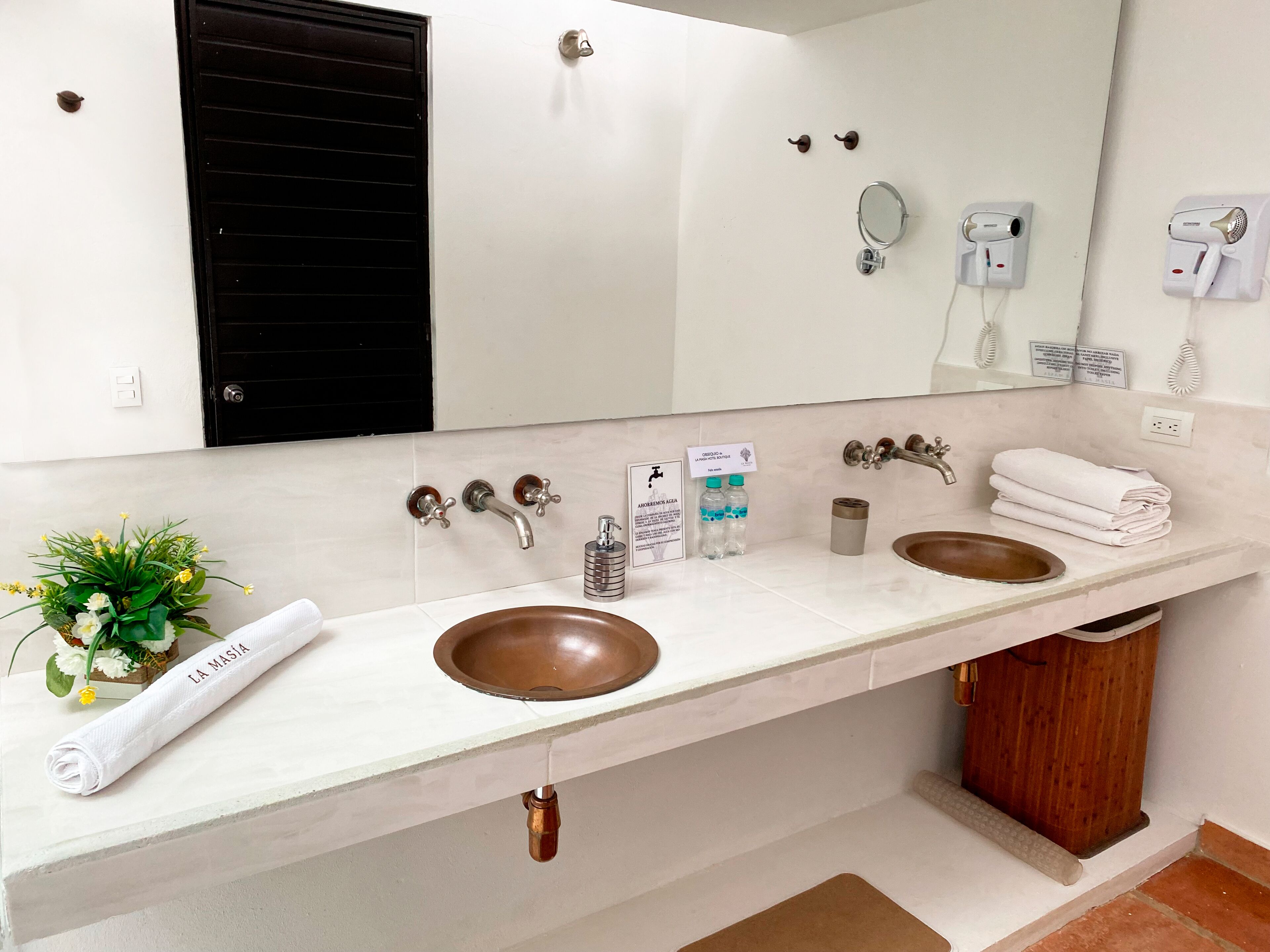 A bathroom with two sinks, a mirror, a towel, a plant, and a sign.