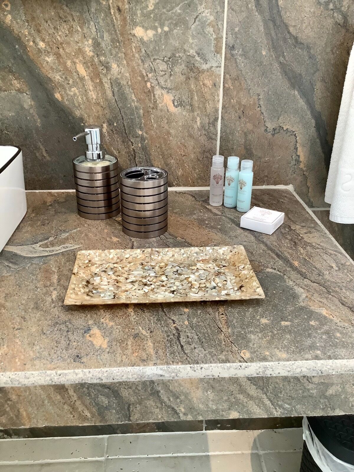 Una encimera de baño con un dispensador de jabón, dos recipientes cilíndricos y tres botellas de jabón líquido.