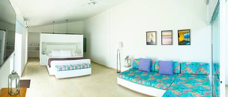 A modern bedroom with a bed, a sofa, and a nightstand. There are ceiling fans, a floor lamp, and a window with blinds.
