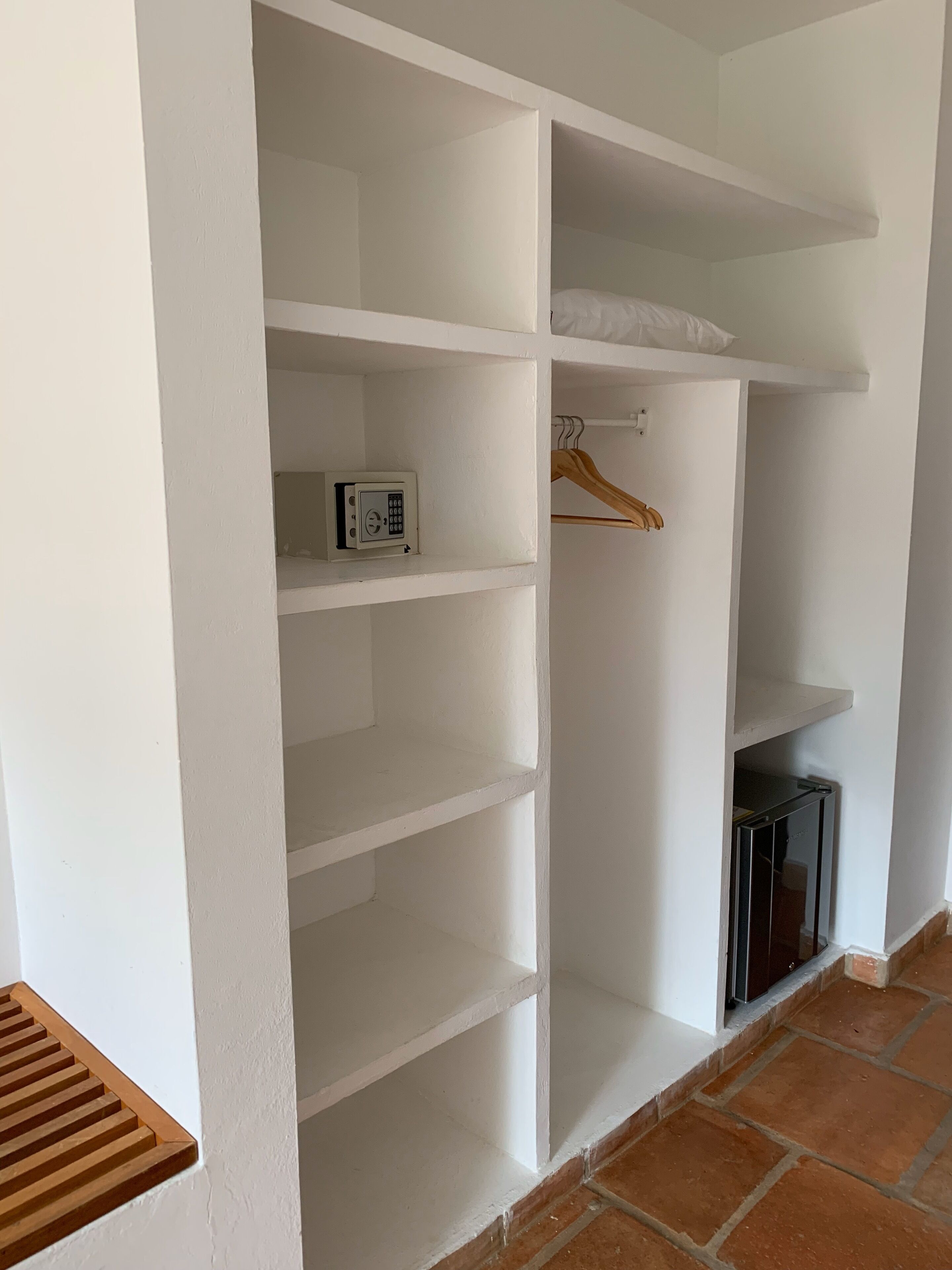 Interior blanco con armario empotrado que incluye varios estantes, una barra para colgar y un pequeño dispositivo electrónico en uno de los estantes.