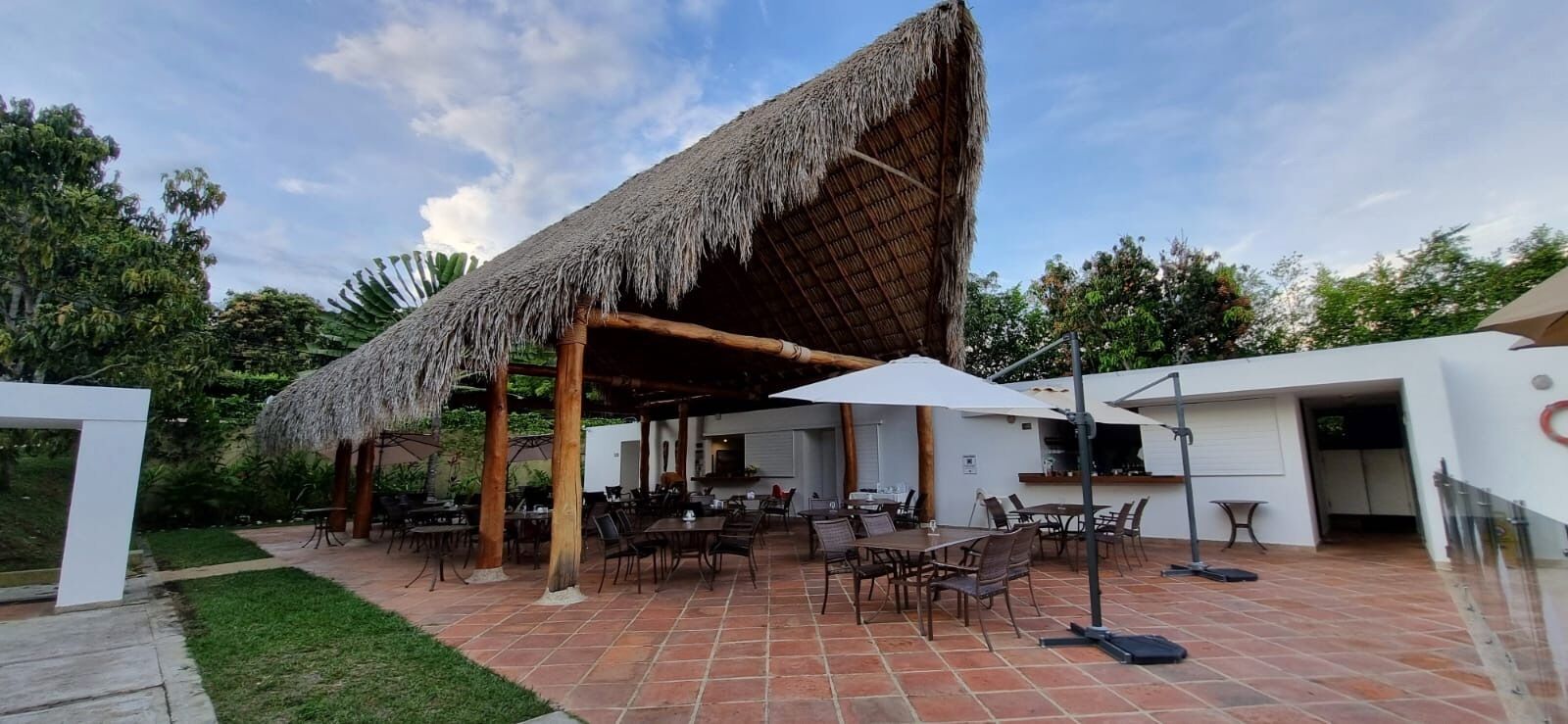 Un patio exterior con asientos, mesas y sombrillas de techo de paja.