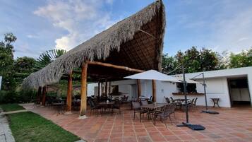 Un patio exterior con asientos, mesas y sombrillas de techo de paja.