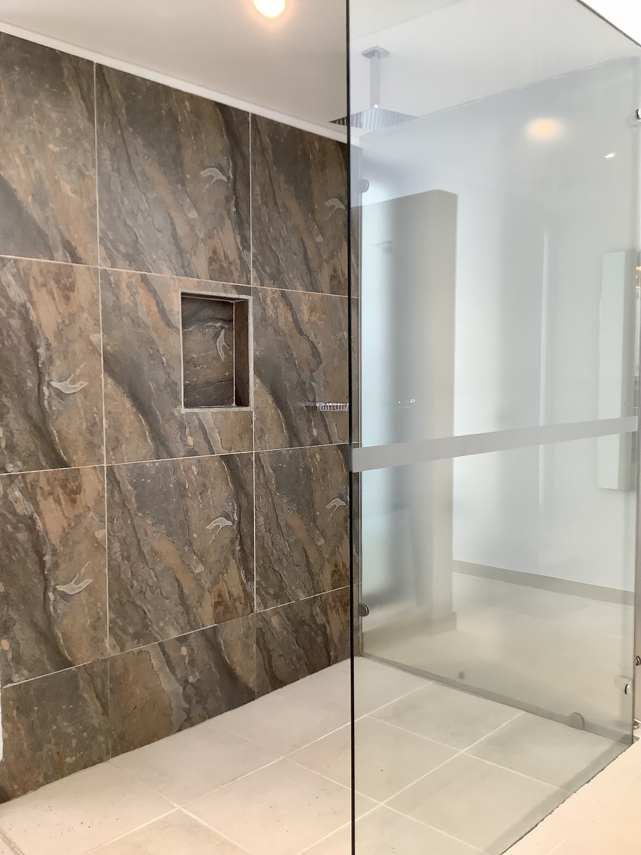 A modern bathroom with a glass shower enclosure, marble tiles, and a small square tile feature on the wall.