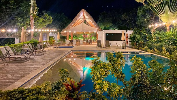 A nighttime outdoor pool area with lounge chairs, a thatched-roof structure, and string lights. - LA MASIA HOTEL BOUTIQUE (Anapoima)
