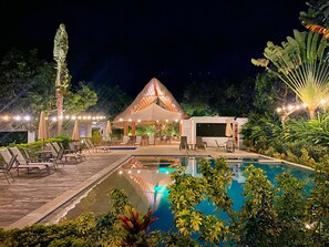 A nighttime outdoor pool area with lounge chairs, a thatched-roof structure, and string lights. - LA MASIA HOTEL BOUTIQUE (Anapoima)