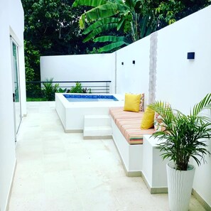 Terrassa exterior moderna amb una paret blanca, una piscina petita, zona de seients amb coixins i una planta en test.