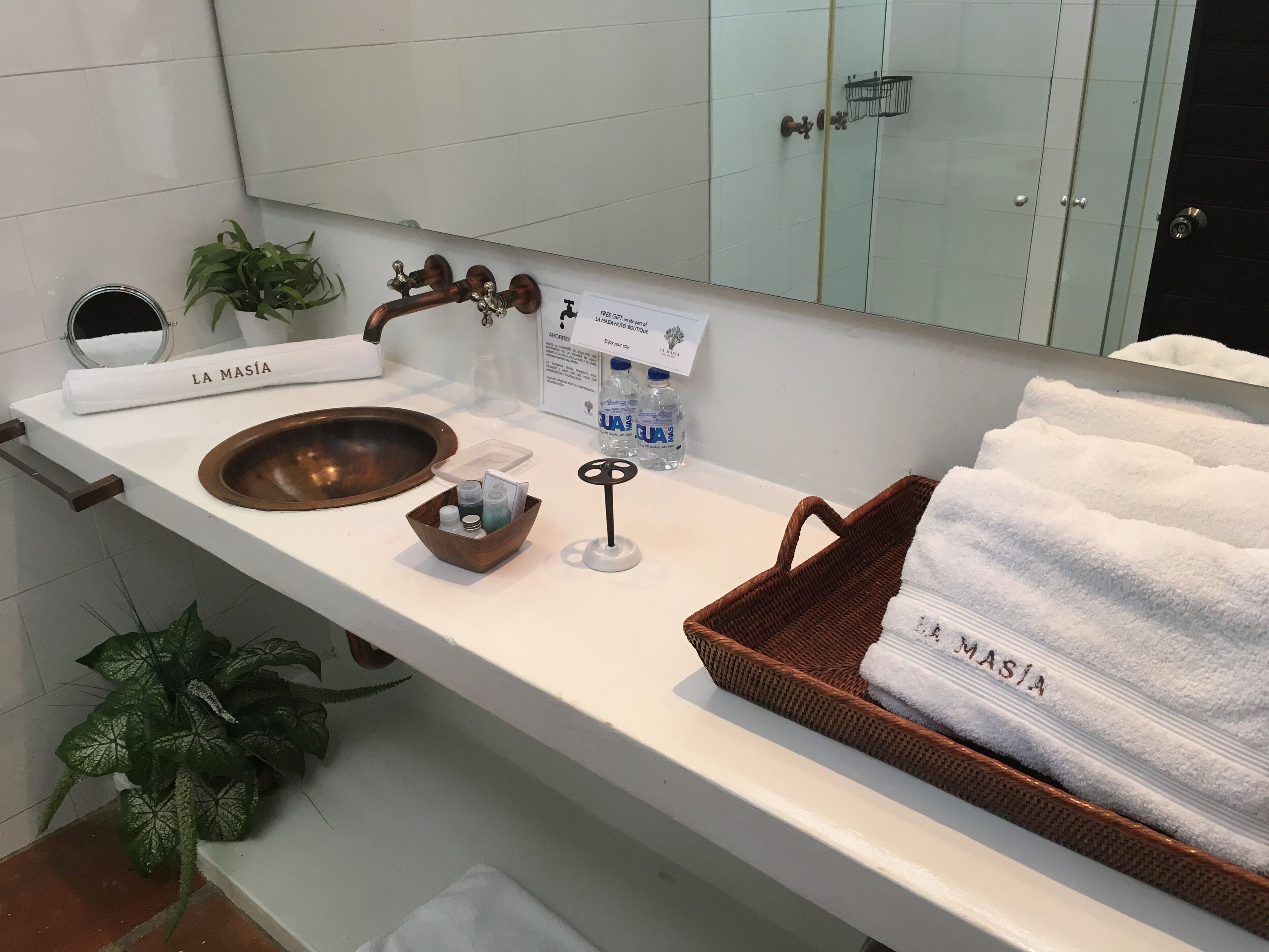 A bathroom with a wooden sink, a towel rack labeled "LA MASIA", a small wooden basket, and a bottle of water.