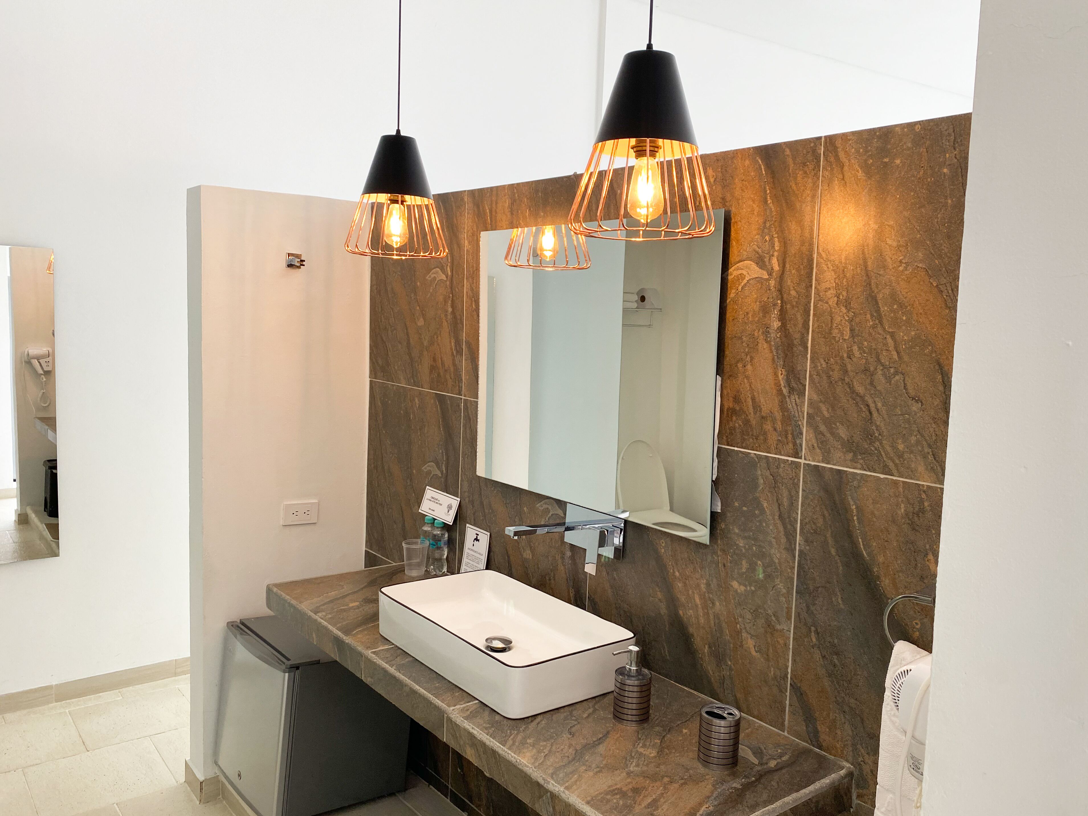 A modern bathroom with a marble backsplash, a white sink, and two pendant lights.