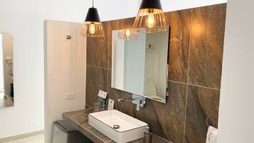 Une salle de bain moderne avec un pare-feu en marbre, un lavabo blanc et deux luminaires suspendus.