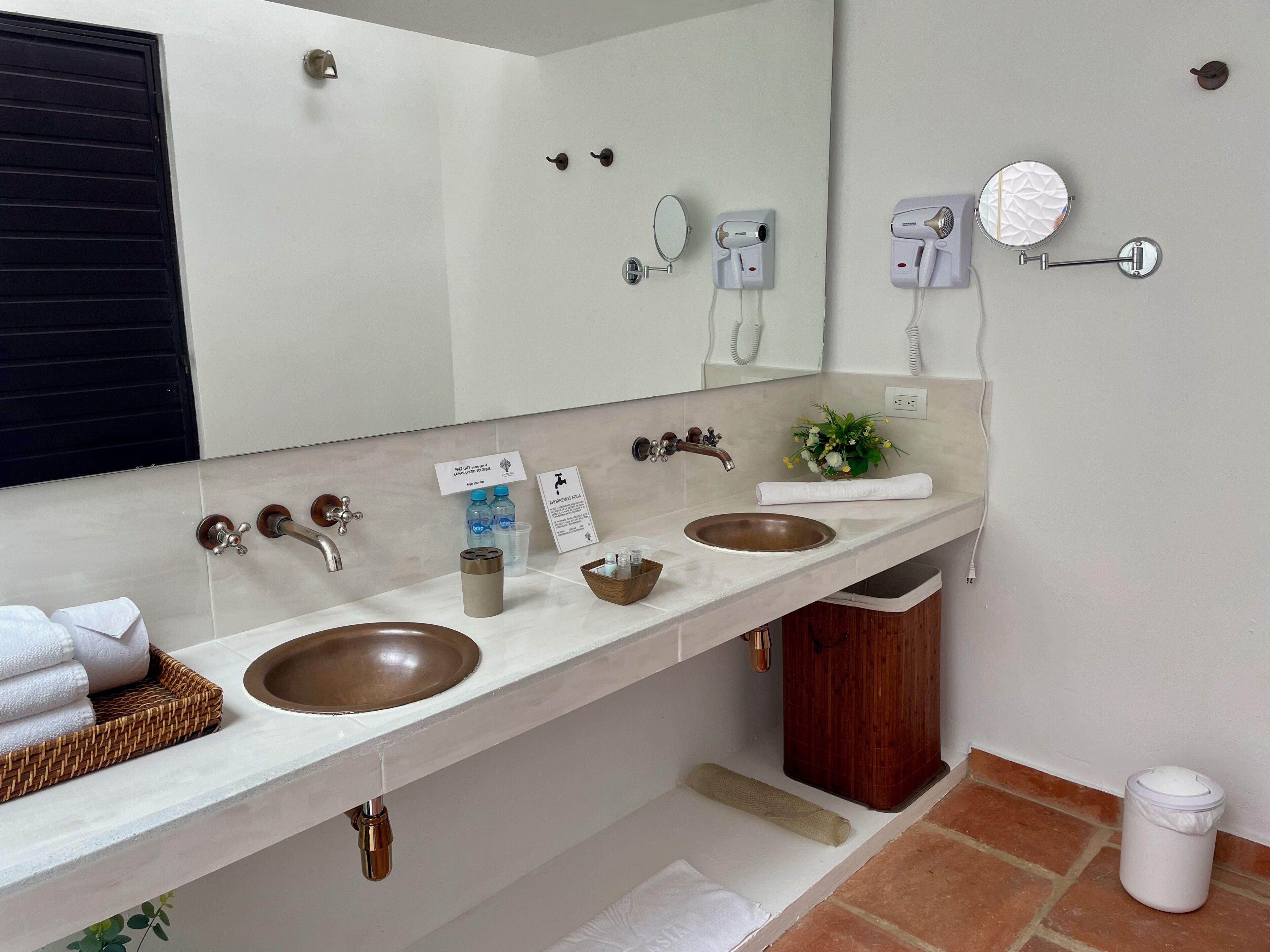 A bathroom with two sinks, a mirror, a towel rack, and a trash bin.