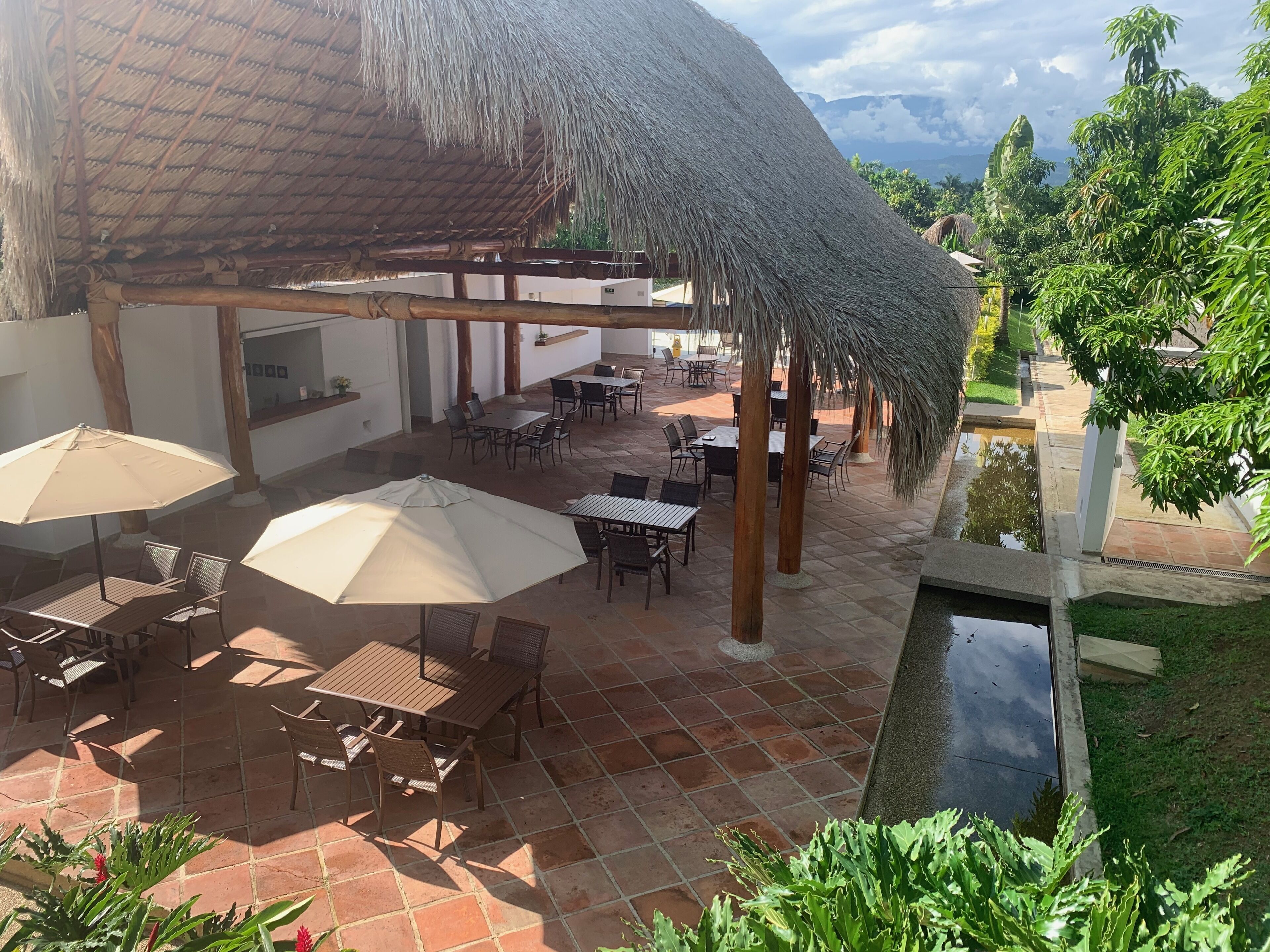 Un espacio de patio al aire libre con construcciones de techo de paja, mobiliario exterior y una pequeña fuente de agua.