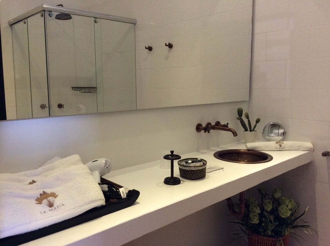 Baño con tocador blanco, espejo, lavabo con grifo de cobre, toallero y planta en maceta.