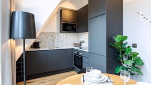 A modern kitchen with dark grey cabinets, a microwave, a toaster, and a wooden dining table set with plates, glasses, and cutlery. - Coleherne Road Residence X (London)