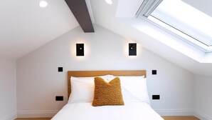 A bedroom with a sloped ceiling, a skylight, a wooden headboard, and two wall-mounted light fixtures. - Coleherne Road Residence X (London)