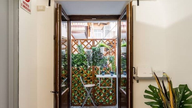 Une porte-fenêtre donnant sur un petit espace extérieur agrémenté d’une clôture en treillis de bois, d’une chaise et d’une table sur laquelle est posée une plante en pot.