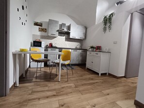A compact kitchen with white cabinets, a dining table with two chairs, and a hanging plant. - Centro Città My House (Catania)