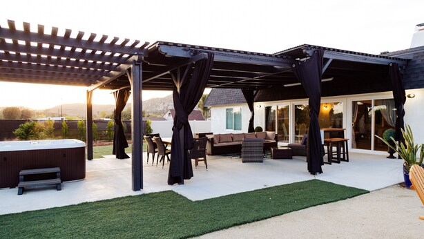 A covered patio area with outdoor seating, a hot tub, and artificial grass. - Rainbow Canyon Retreat:  Hot Tub, Fire Pit, Games Room - Sleeps 16+ (Fallbrook)