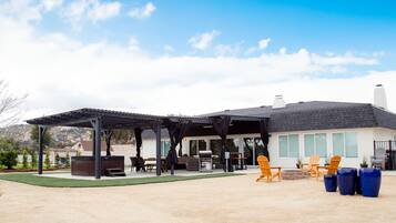 A covered patio area with outdoor furniture, a barbecue grill, and a large window overlooking the backyard.
